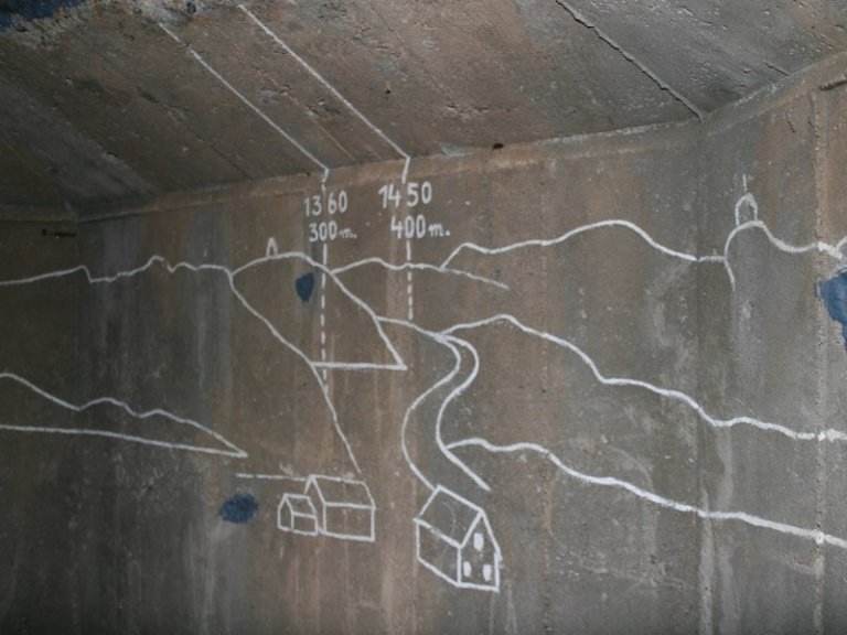 Tegning på betongvegg som viser landskap med fjell, hus og elv, med to sett målinger skrevet på veggen.